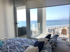 Une chambre avec une grande fenêtre donnant sur une plage et le paysage urbain.