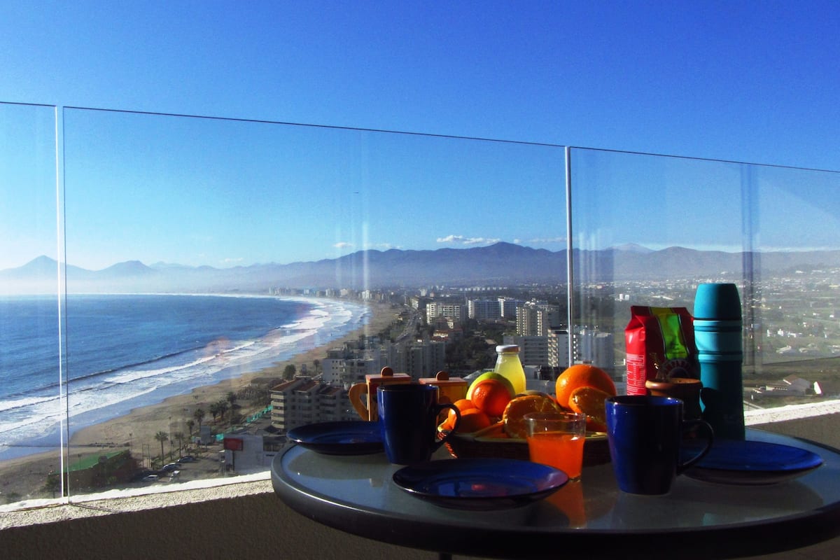 A table with a glass partition overlooking a beach and cityscape.