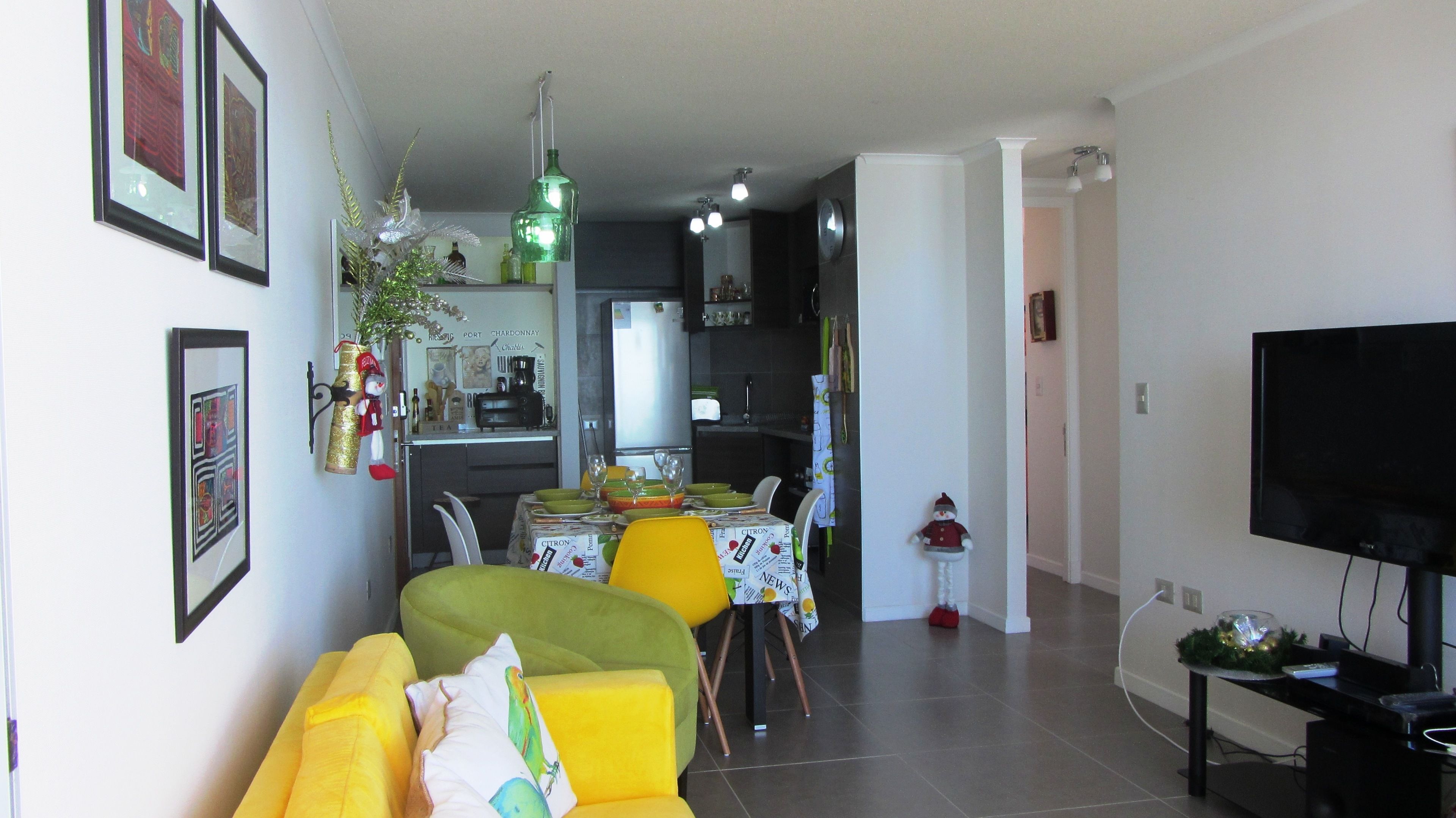 Una sala de estar moderna con un sofá verde, una mesa de comedor con sillas amarillas y una cocina al fondo.