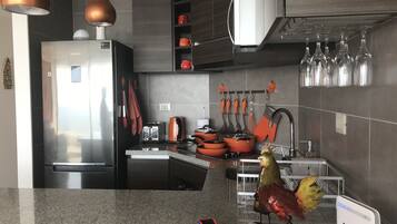 Una cocina moderna con un refrigerador de acero inoxidable, un tostador y una cafetera. Hay ollas y sartenes naranjas en la encimera, y una decoración de gallo en la pared.