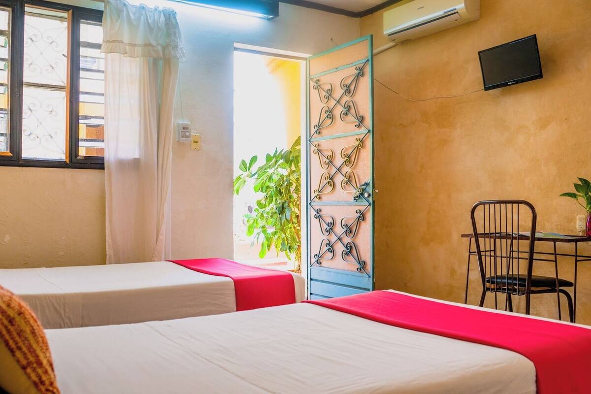 A room with two beds, a table with a chair, and a TV on the wall.
