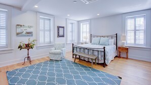 A bedroom with a large bed, a chair, a bedside table, and a window with shutters. - Exclusive Property Just Steps from History & Culture (Charleston)