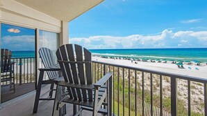 Een balkon met twee Adirondack stoelen, uitkijkend op een strand met parasols en ligbedden.