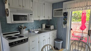 Une cuisine de taille réduite avec des meubles blancs, un four à micro-ondes, une cuisinière et un évier. On y trouve également une poubelle et une table à manger avec des chaises.