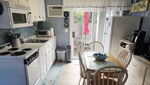 A compact kitchen with white cabinets, a microwave, a stove, and a dining area with a table and chairs. - Cozy studio only 3/10 of a mile from Nantucket Sound, Free WIFI (Dennis)