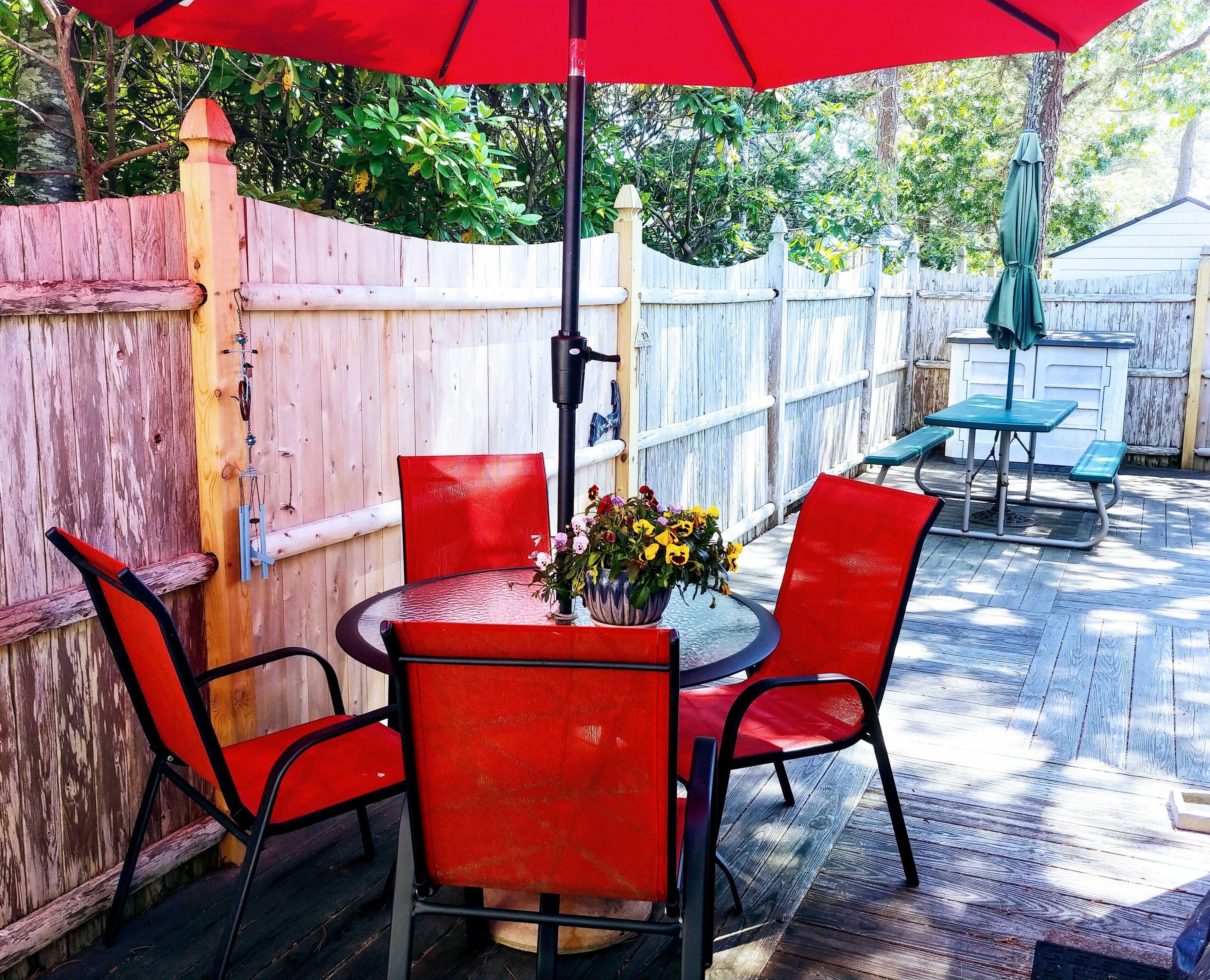 Eine Terrasse mit einem runden Tisch, roten Stühlen und einem roten Sonnenschirm.