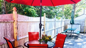 A patio with a round table, red chairs, and a red umbrella. - Cozy studio only 3/10 of a mile from Nantucket Sound, Free WIFI (Dennis)
