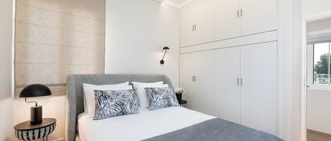 Un dormitorio moderno con una cama grande, un armario blanco y una lámpara de noche.