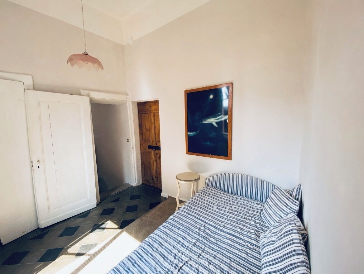 A bedroom with a bed, a door, a small stool, and a framed picture on the wall.