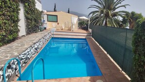 Una piscina rectangular amb vora de pedra i rajola, envoltada per un camí de pedra i una tanca verda.