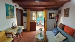 Un saló acollidor amb un sofà, una taula de dinar amb cadirees, un televisor i una porta que dona a un balcó.