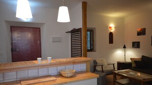 Een keuken met een houten aanrecht, een eethoek met een tafel en stoelen, en een woonkamer met een bank en een lamp.