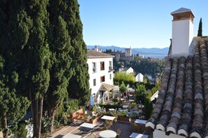 A courtyard with outdoor seating, a white building with a tiled roof, and a view of distant mountains. - A beautiful and comfortable historic home with a view of the Alhambra in Granada / Albayzin (Granada)