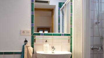 Un baño con lavamanos blanco, espejo y ducha.