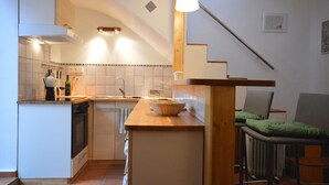 Een compacte keuken met een houten kookeiland, een ingebouwde oven en een klein zithoekje met een stoel.
