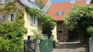 A narrow street with a yellow house with shutters, a green gate, and a red-tiled roof building.
