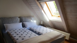 A bedroom with a bed, two pillows, a bedside table, a radiator, and a window.