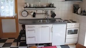 A compact kitchen with white cabinets, a sink, stove, and a clock.