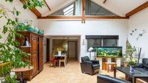 Un vaste espace de vie doté d’un haut plafond, de poutres en bois, d’une table à manger, de chaises, d’un canapé, d’un téléviseur et d’un aquarium.