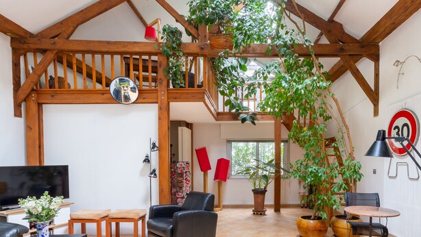 Un vaste espace de vie doté d’un plafond en bois, d’un téléviseur, de sièges confortables et de plantes en pot.