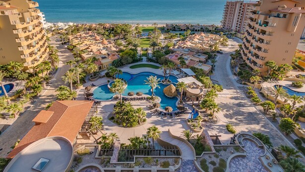 Een resort met meerdere zwembaden, palmbomen en uitzicht op het strand.