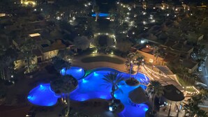 Een nachtzicht van een resort met een centraal zwembad, palmbomen en verlichte paden.