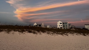 A coastal landscape with a sandy beach and a row of white buildings with flat roofs.