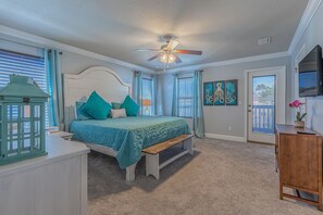 A bedroom with a bed, a ceiling fan, a nightstand, a lamp, and artwork on the wall.
