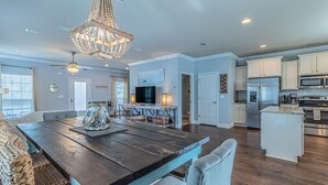 A spacious kitchen with modern appliances, a dining area with a wooden table and chairs, and a chandelier.