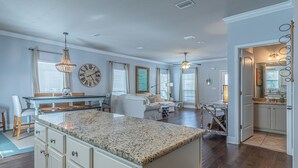 A spacious kitchen with granite countertops, a dining area with a blue table, and a living room with a sofa and a painting.