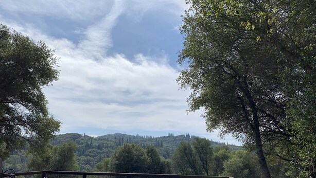 Una terraza de madera con sillas de mimbre y una mesa, con vistas a una ladera boscosa.