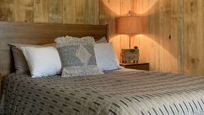 Un dormitorio con paneles de madera, una cama, almohadas y una mesita de noche con lámpara.