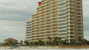 A multi-story hotel with a curved facade, numerous balconies, and a beach view.