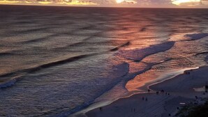 A beach scene with waves and people walking along the shore.