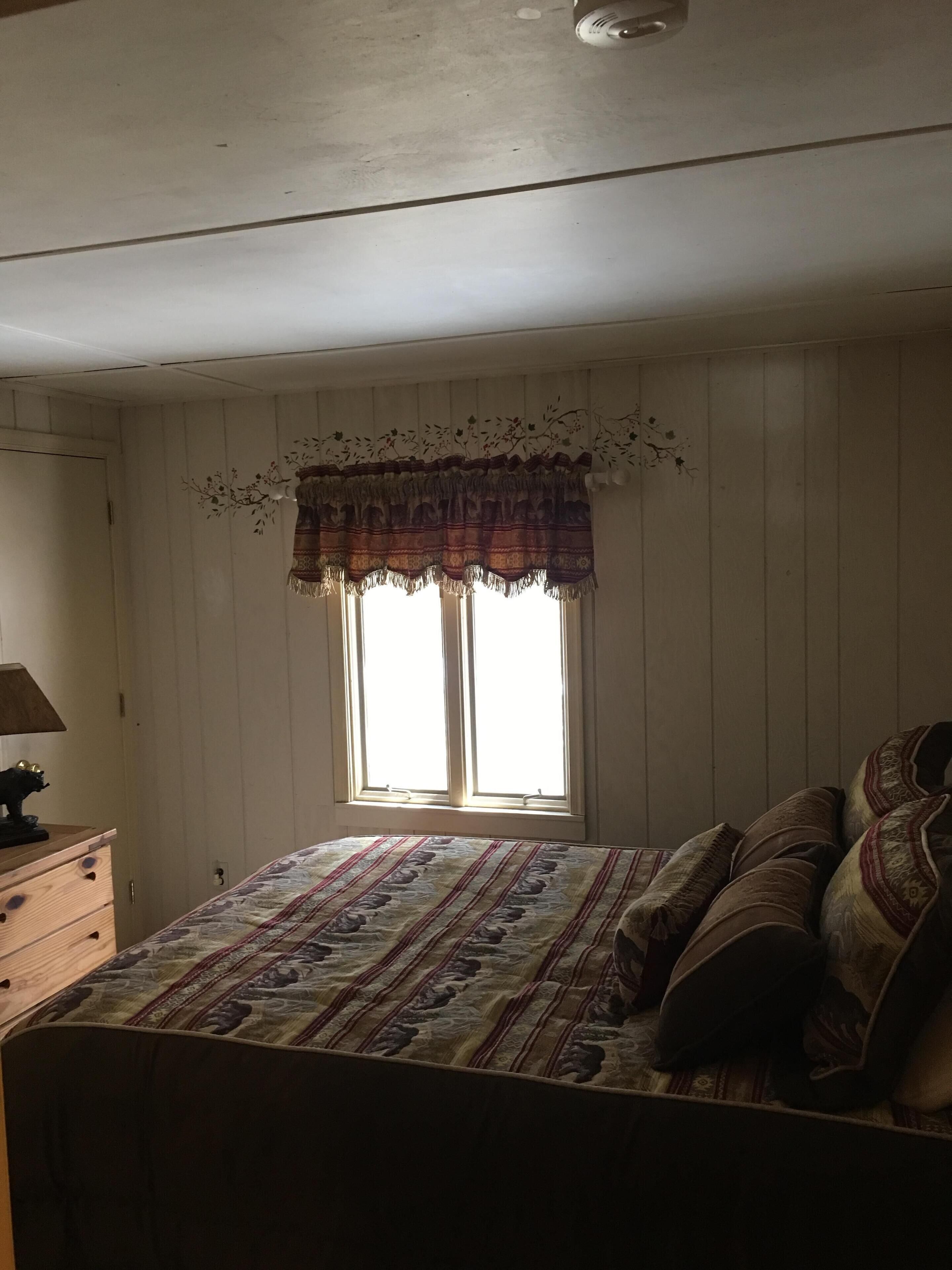 A bedroom with a bed, a dresser, and a window with curtains.