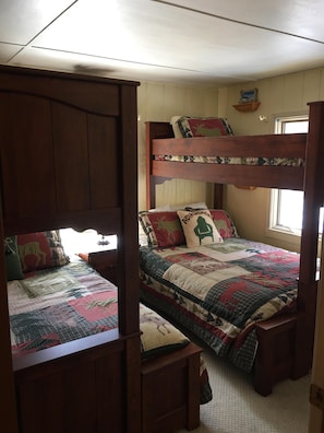 A room with a bunk bed, a lower bed, and a wooden wardrobe.