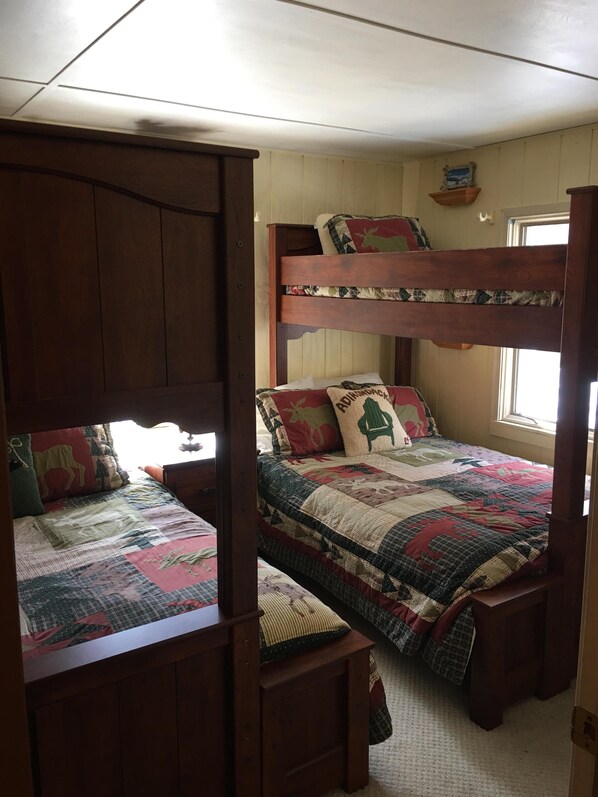 Une chambre avec un lit superposé, un lit simple et une armoire en bois.