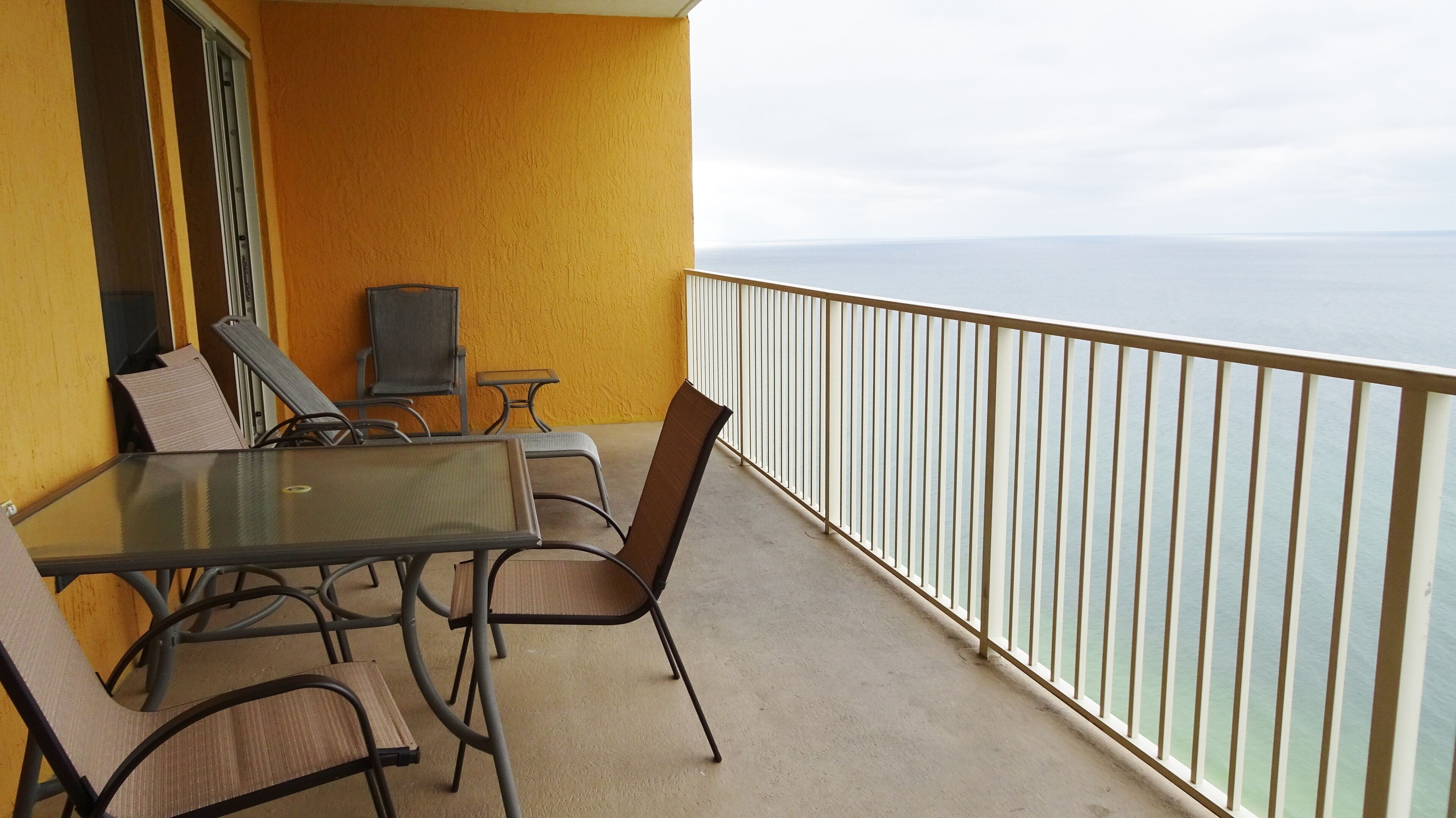 A balcony with a table and chairs, a small TV, and a view of the ocean.