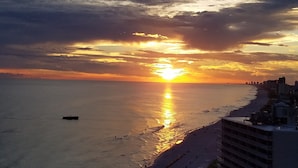 Atardecer sobre una ciudad costera con vistas despejadas al océano y un barco en el agua.