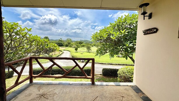 Vista desde un acceso cubierto con barandilla de madera, que da a un espacio verde con árboles y cielo despejado.