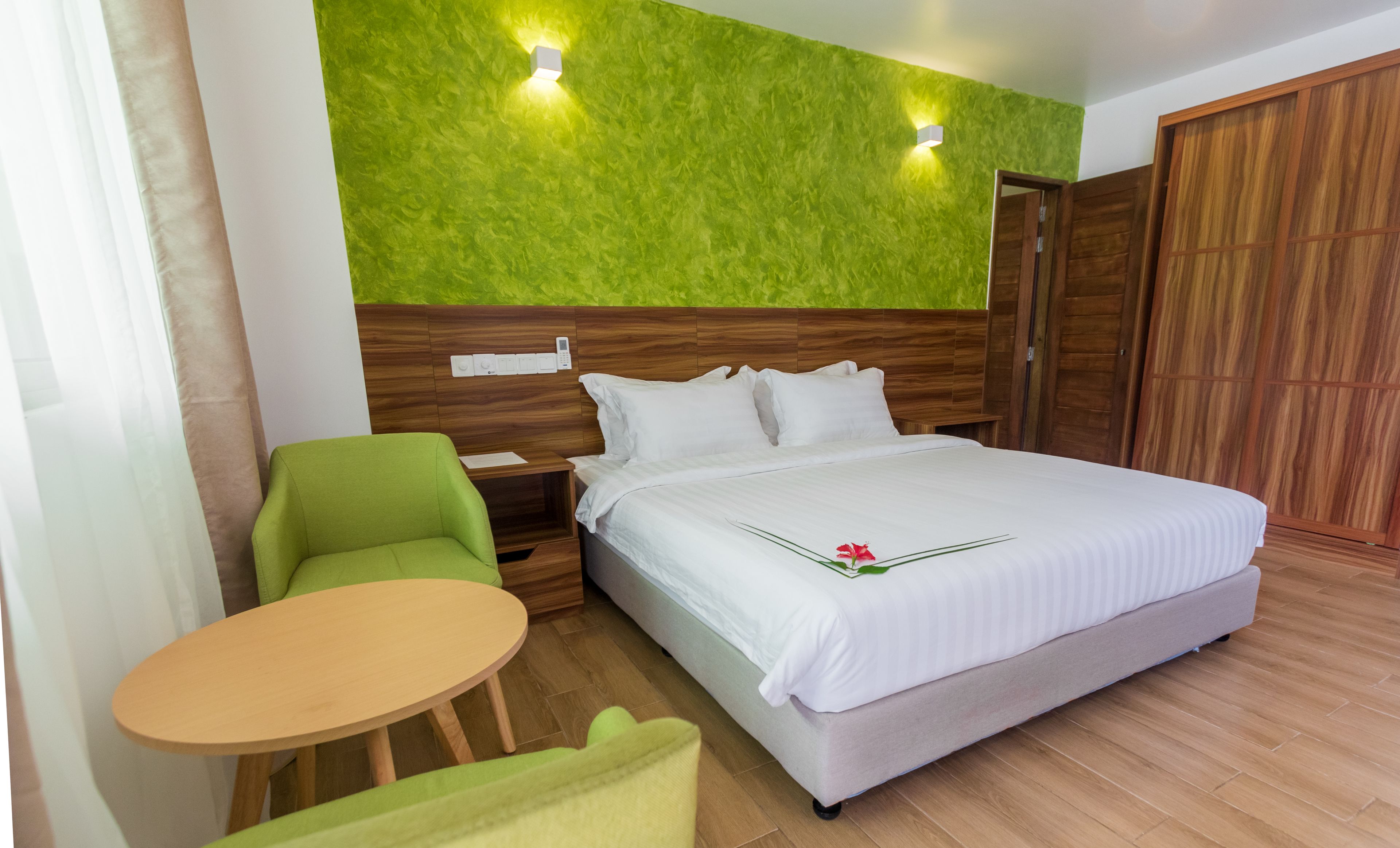 Een hotelkamer met een bed, een groene stoel, een klein rond tafeltje en een garderobe.