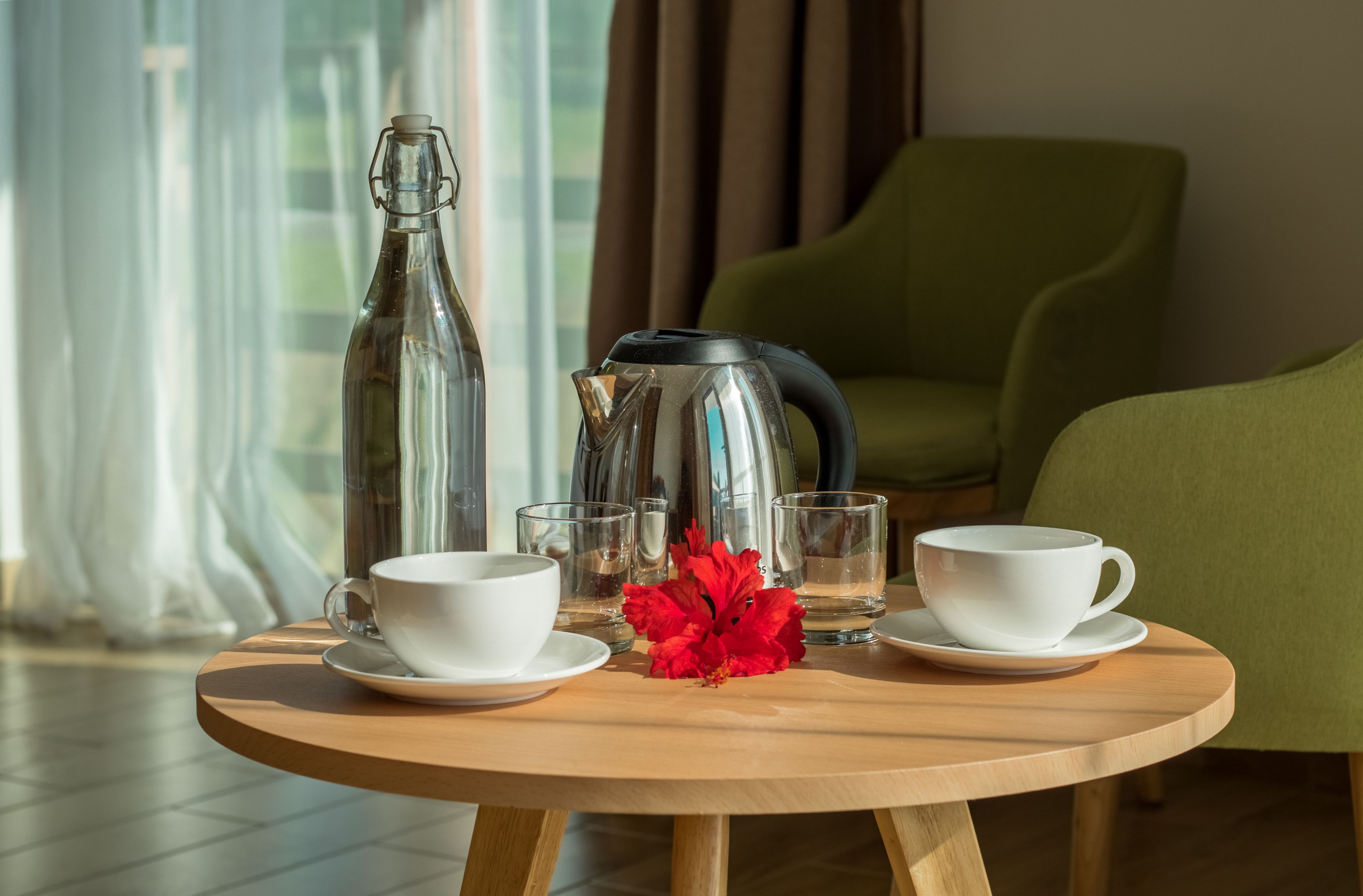 Una mesa de madera con una cafetera, dos tazas y una flor.
