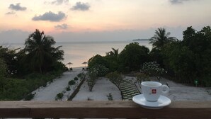 A view of a beach with a cup of tea on a balcony.