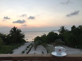 A view of a beach with a cup of tea on a balcony.