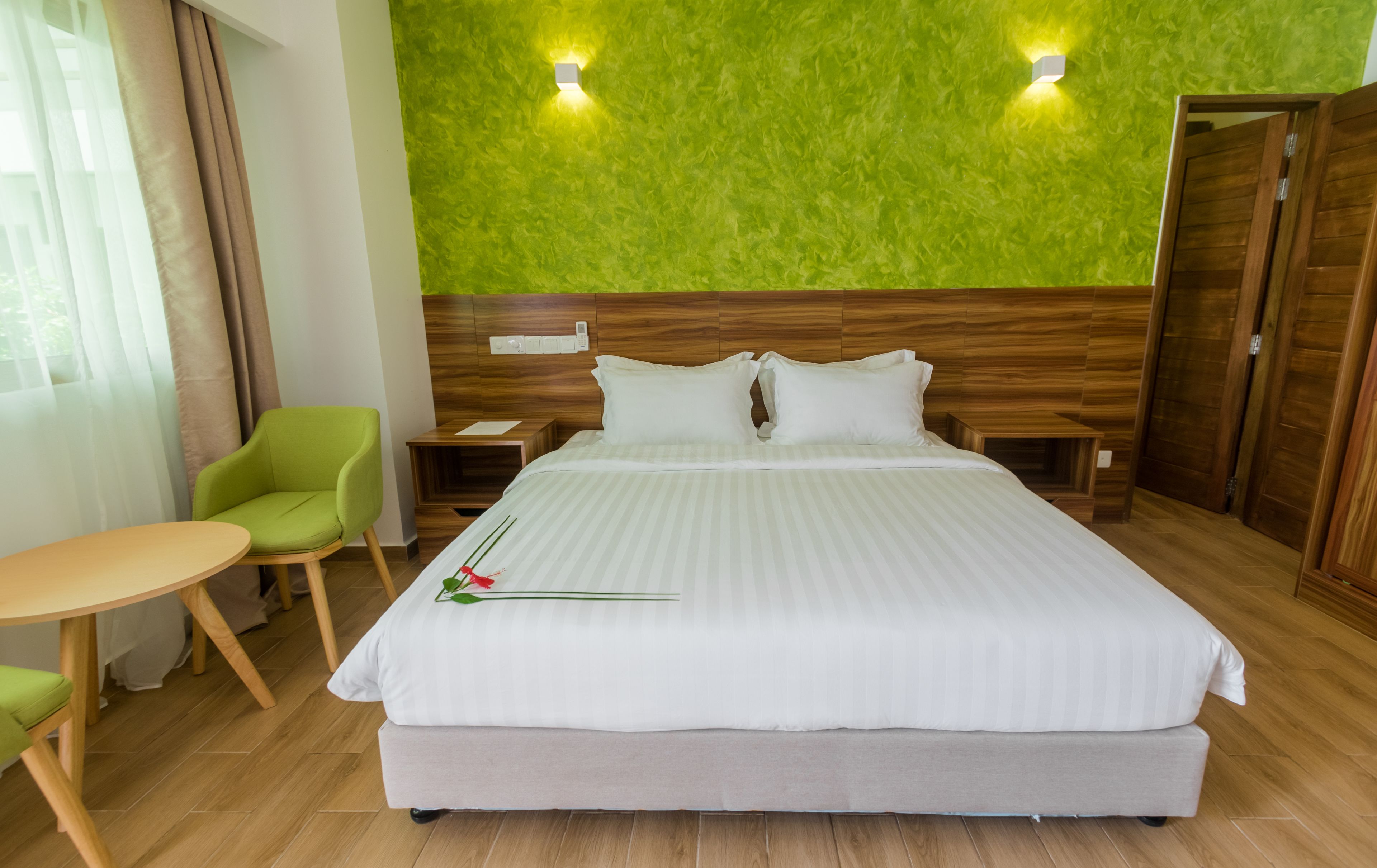 A hotel room with a large bed, a green chair, a small table, and a wooden wardrobe.