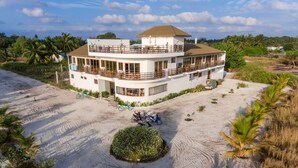 A two-story building with a balcony, surrounded by sand and palm trees.