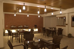 A restaurant with brick walls, multiple tables and chairs, and hanging pendant lights.
