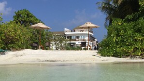 A kayak with a yellow paddle, a sandy beach, and a building with a balcony in the background.