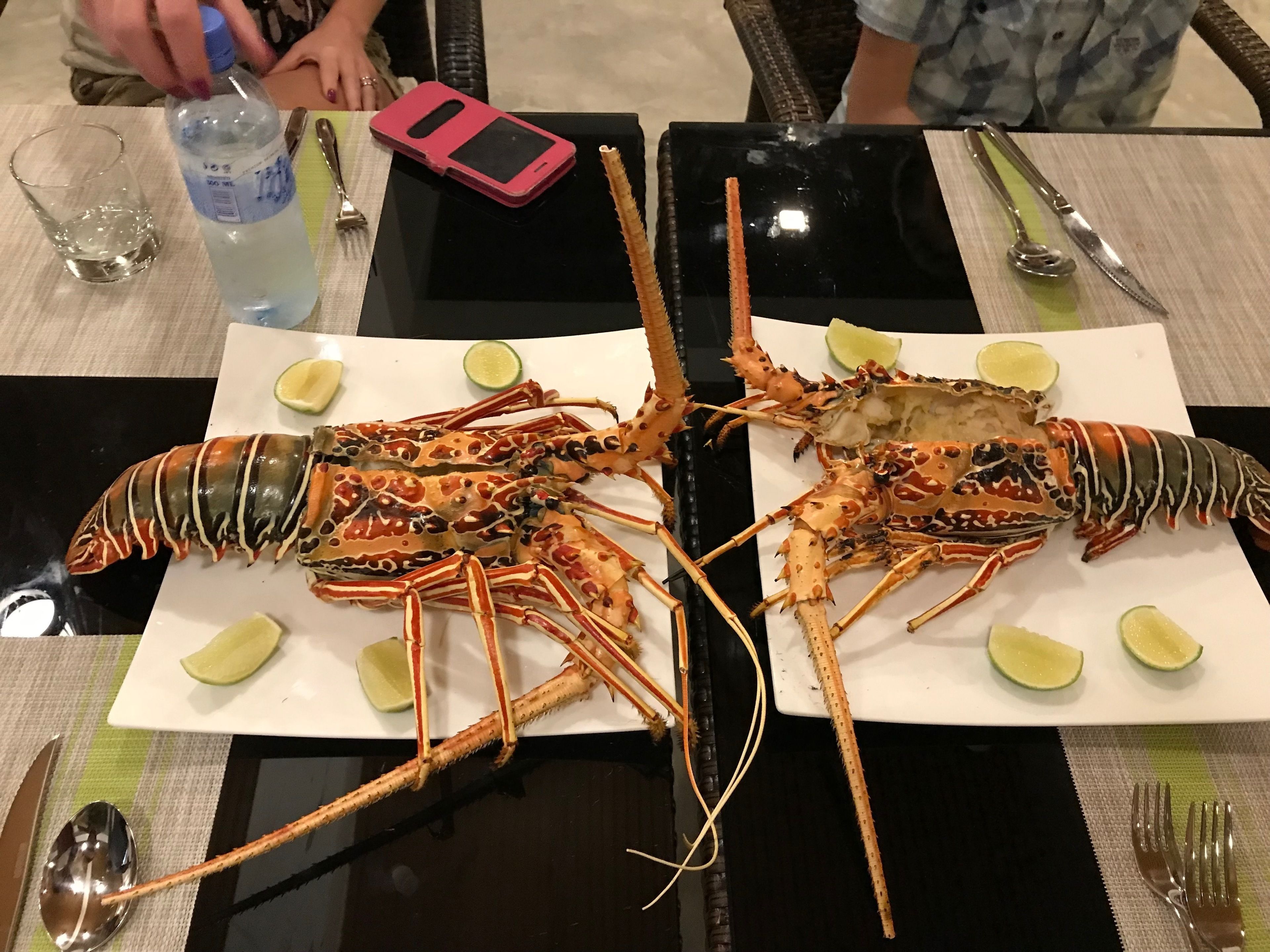 Una mesa de comedor con dos langostas grandes, cuñas de lima y una botella de agua.