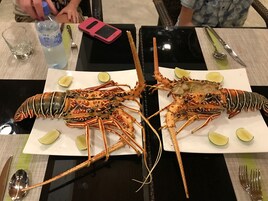 A dining table with two large lobsters, lime wedges, and a bottle of water.